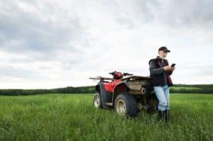 Man using phone leaning on four wheeler in a field