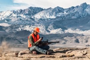 Hunter reading sms marketing while hunting on a mountain.